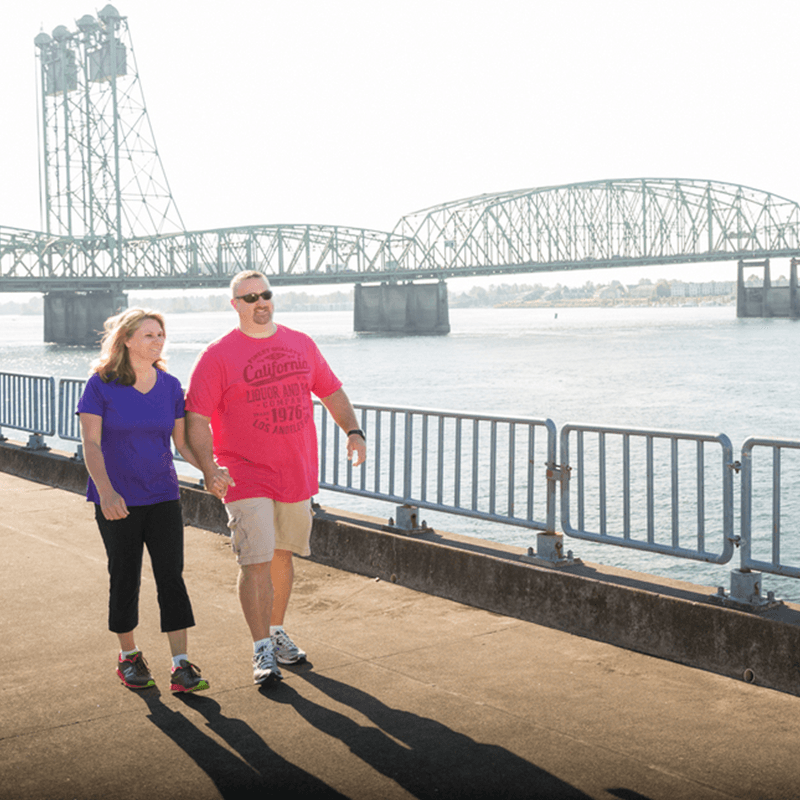 Mature couple walking alongside the Columbia River with the I-5 bridge in the background