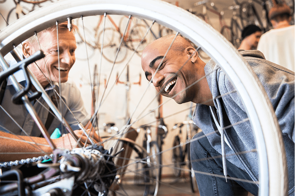Two gentlemen laughing while working on a bike tire